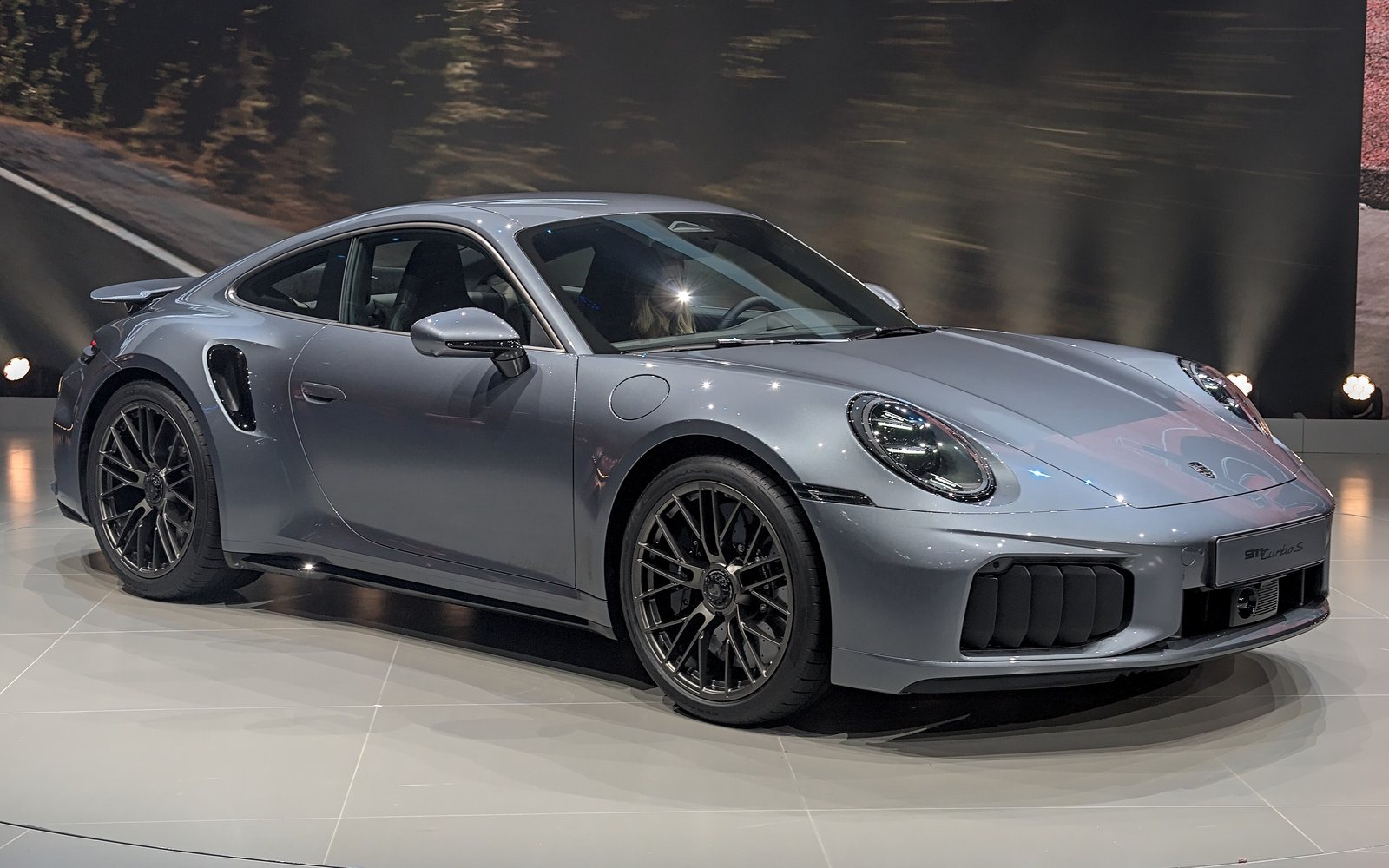 Porsche 911 Turbo S coupe in grey, front three-quarter view on a lit show stage